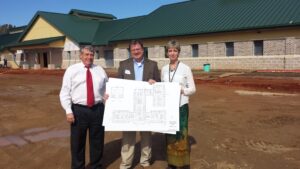 State Director John H. Magill, Architect Bell, and Susan Anderson hold blueprints in front of new SWMHC building.